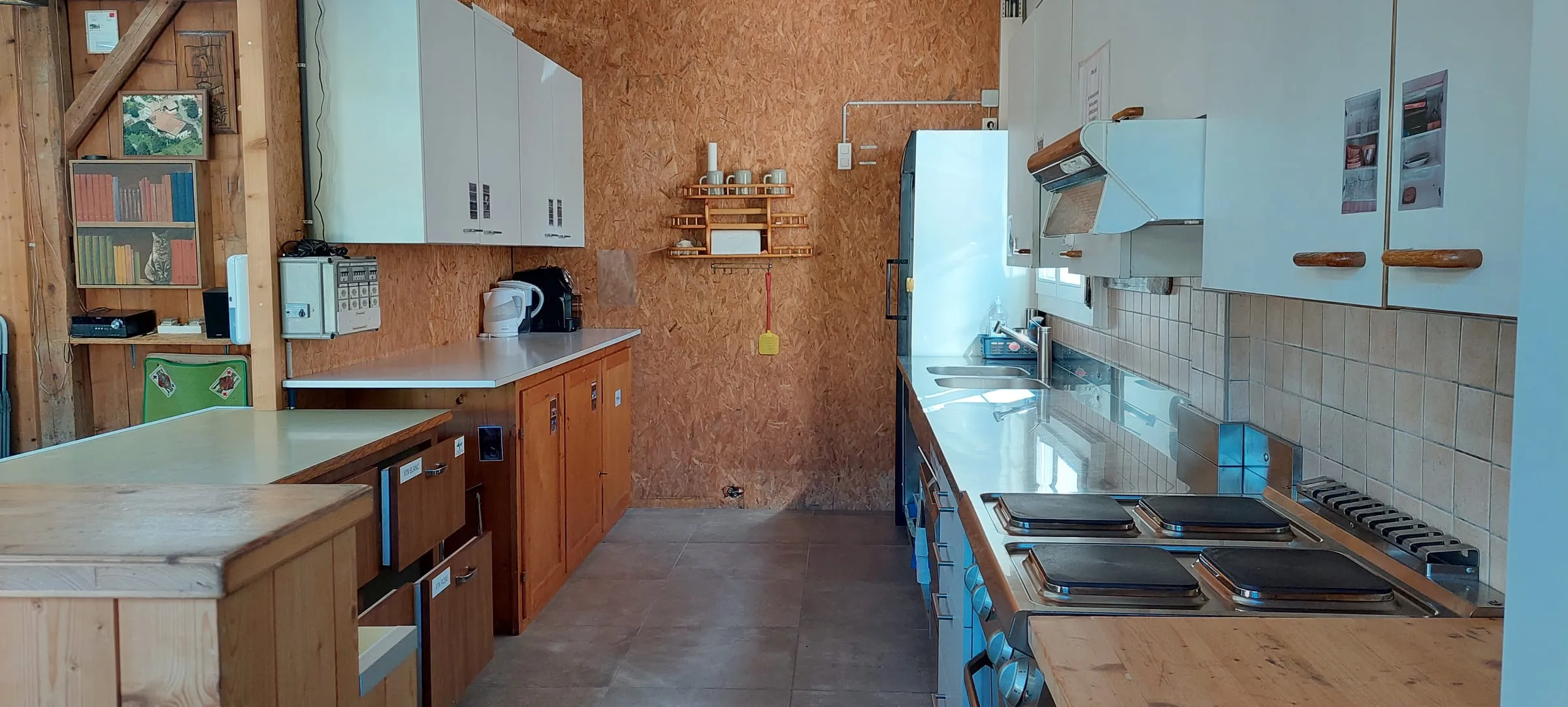 La cuisine sur toute sa longueur : plaques de cuisson, hotte, double évier et plans de travail